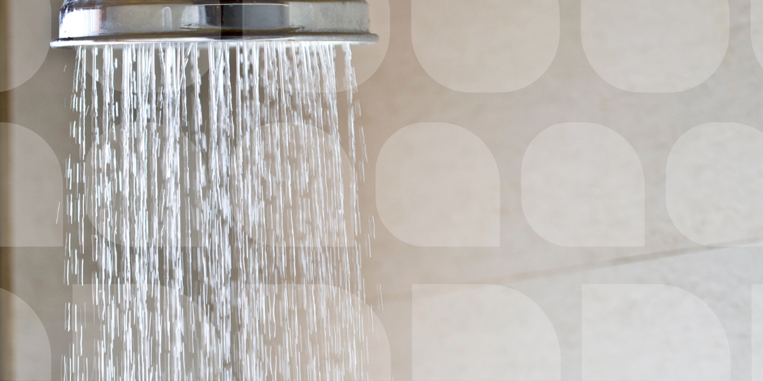 Chrome shower head spraying water against a beige tiled bathroom wall 
