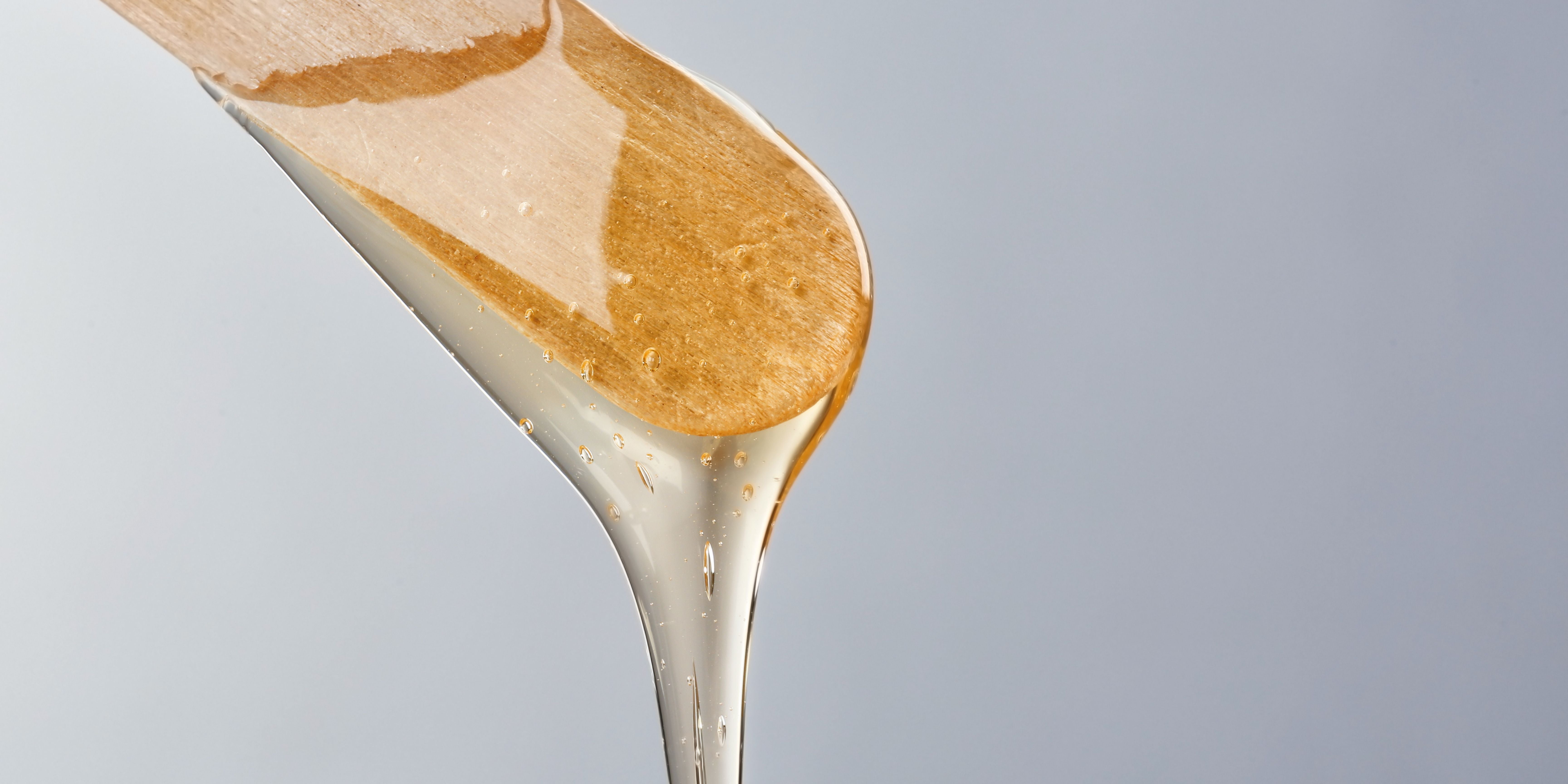 Close up image of hair removing wax dripping off a wooden stick 