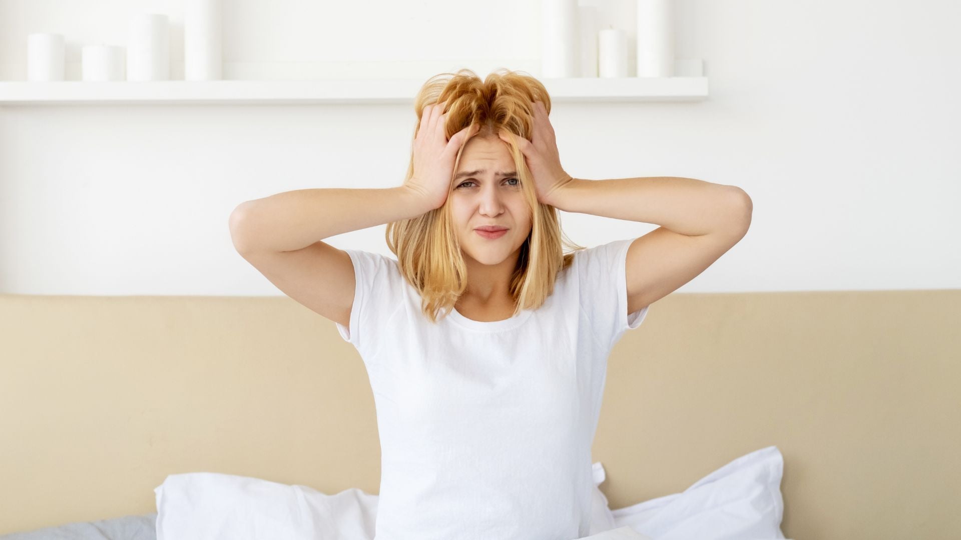 A woman sitting on a bed holding her head