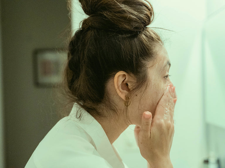 Woman applying cream to her face in a bathroom setting