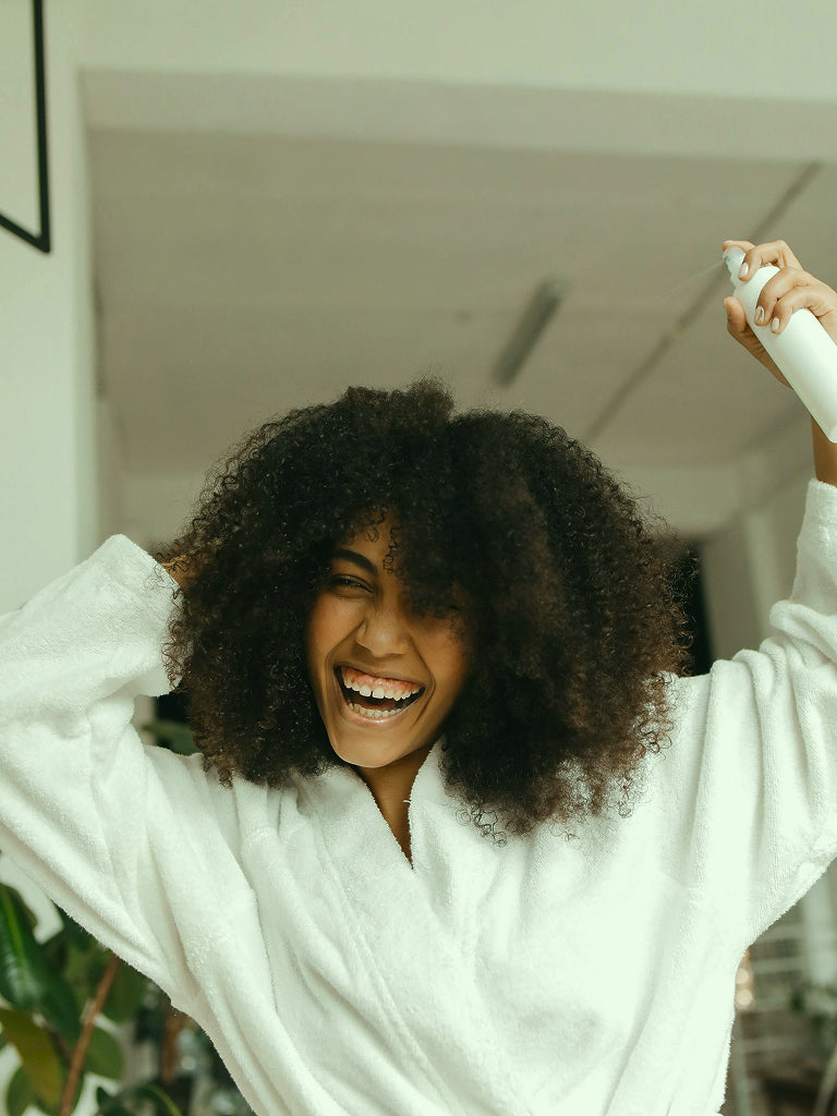 Person in a white robe with curly hair, standing indoors.