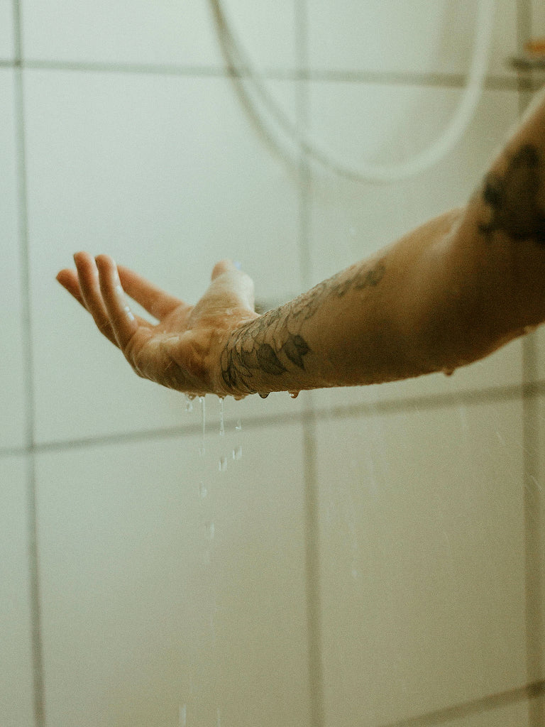 Person's arm with tattoos under a shower with water droplets.