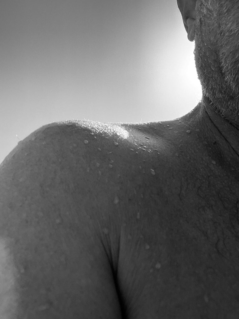 Black and white close-up of a older mans  shoulder with water droplets on him with. a blurred background