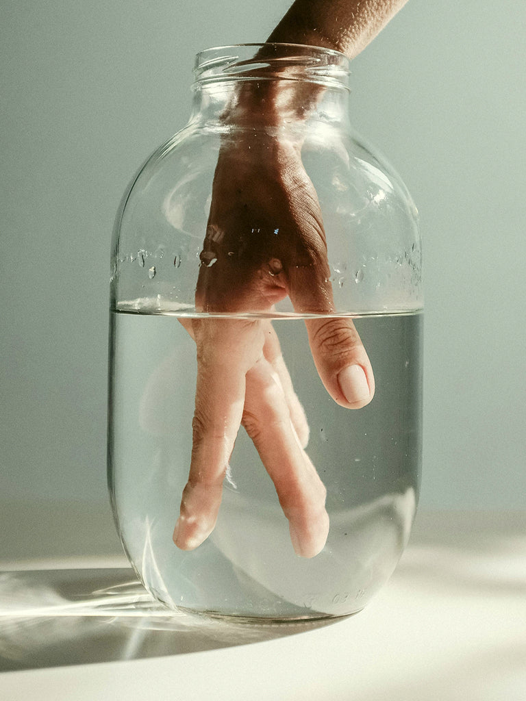 Hand submerged in a jar of water with a neutral background