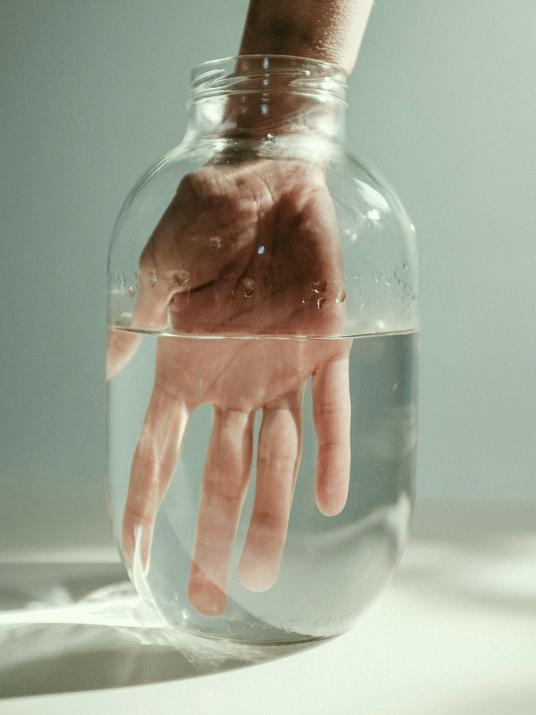 Hand submerged in a jar of water with a blurred background