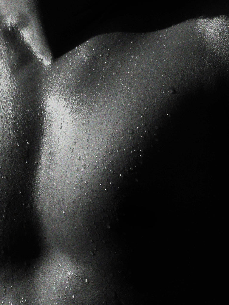 Close-up of a mans chest with water droplets glowing in the light