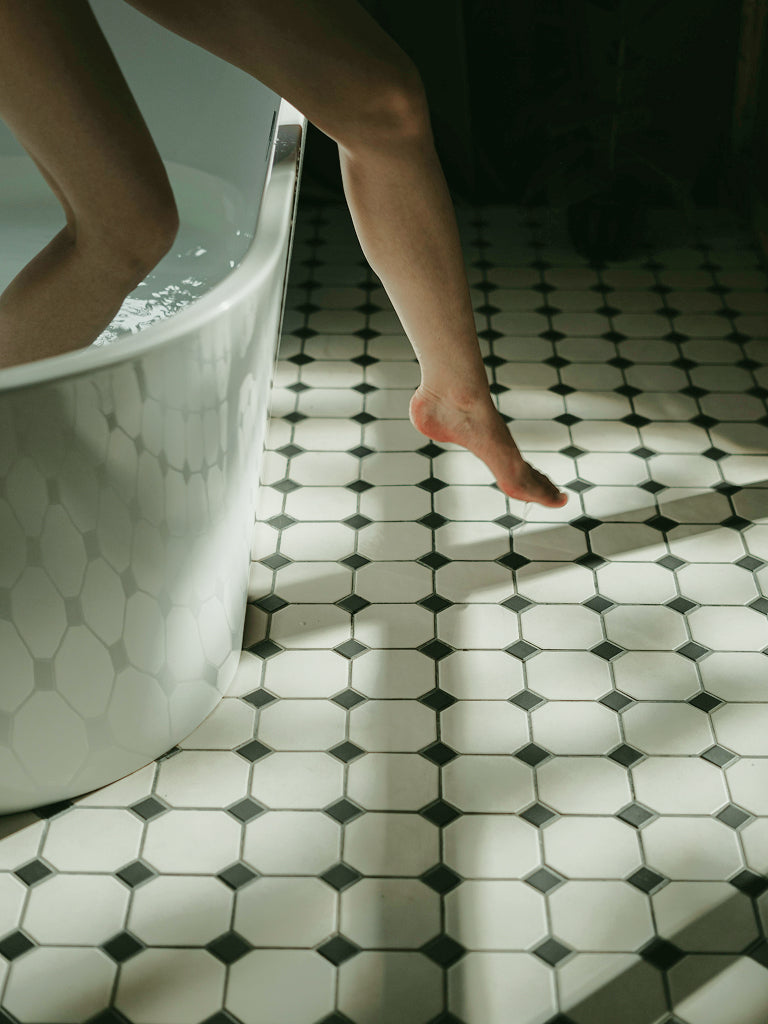 Person stepping out of a bathtub onto a black and white tiled floor