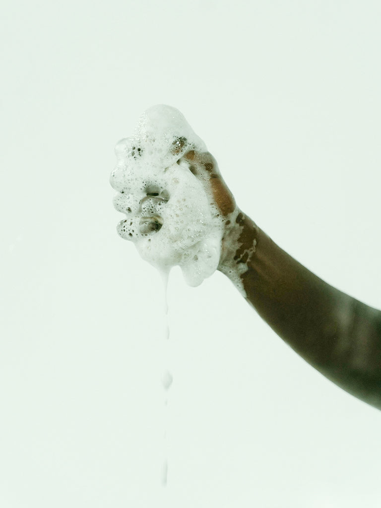 Hand squeezing a loofa lathered in soap  against a white background