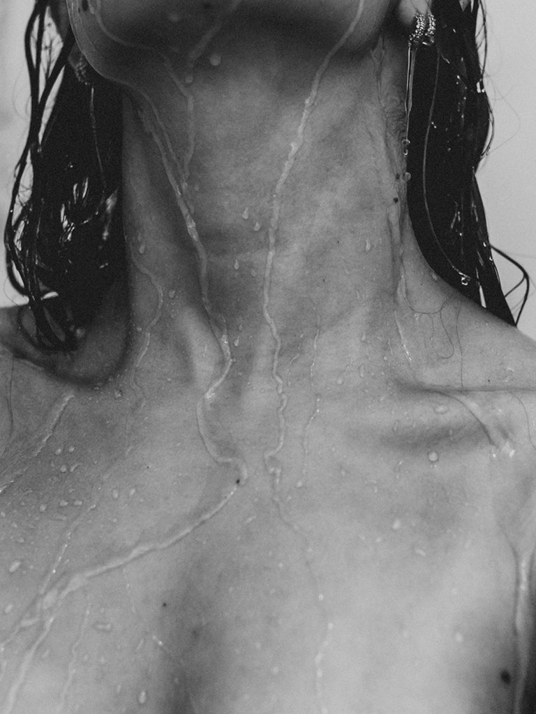 Close-up of a womans neck, shoulders and chest with water streaming down her body.
