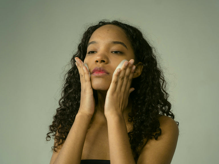 Woman applying cream to her face against a plain background